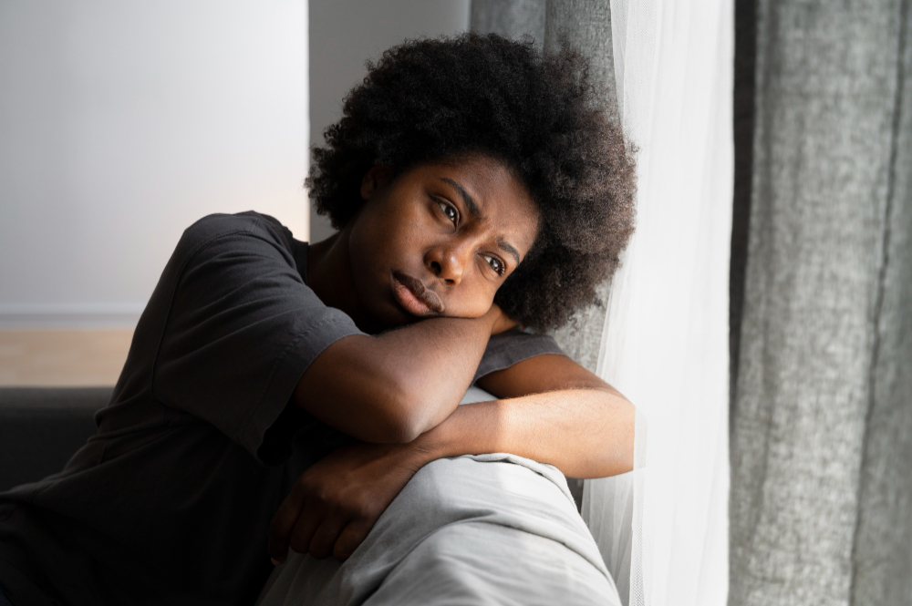 Femme pensive appuyée près d’une fenêtre, illustrant la solitude et la détresse psychologique