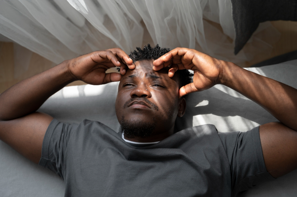 Homme allongé sur un lit tenant sa tête, symbolisant le stress intense et l’anxiété