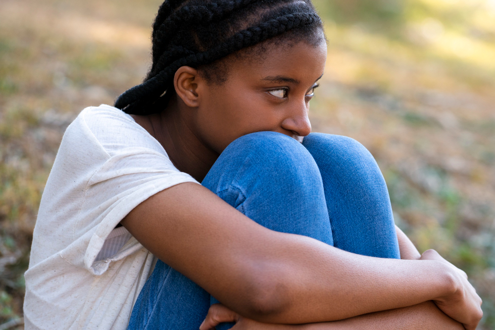 Adolescente assise les genoux contre elle, exprimant la tristesse et la vulnérabilité émotionnelle, illustrant la santé mentale chez les adolescents.